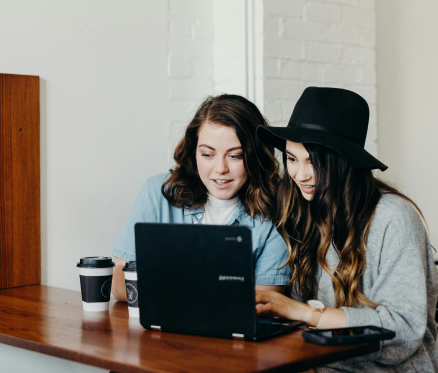 Zwei Frauen schauen gemeinsam auf einen Laptop in einem Café.